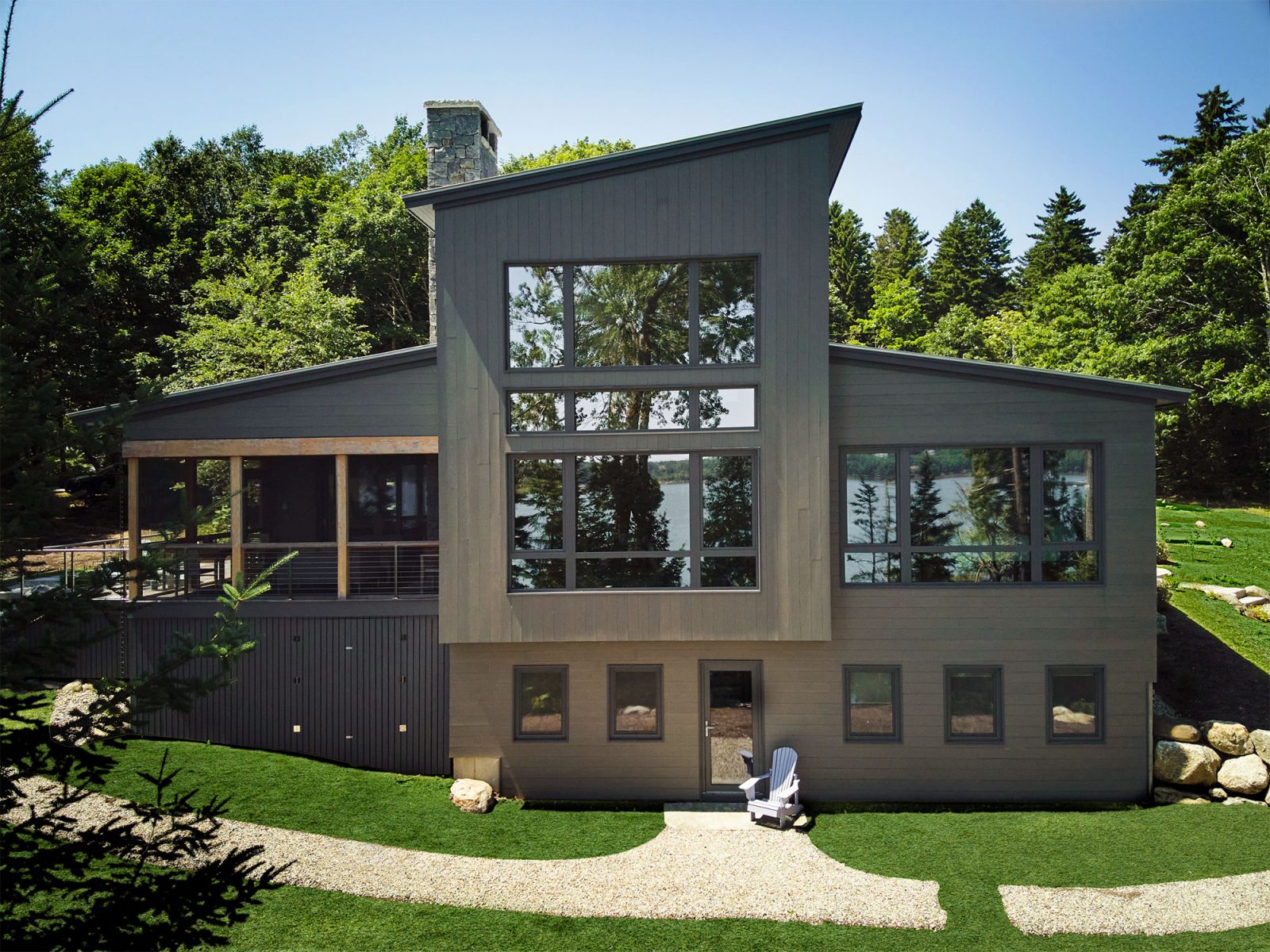 A contemporary, angular home with large windows surrounded by green lawn and trees.